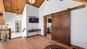 A spacious room with a wooden ceiling, a large sliding barn door, a wooden desk, and a mounted painting. - End Unit  - EV Charger, Fireplace & Jacuzzi (Estes Park)