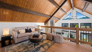 A cozy living room with a high wooden ceiling, a sofa, a coffee table, and a view of the outdoors through large windows. - End Unit  - EV Charger, Fireplace & Jacuzzi (Estes Park)