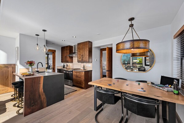 A modern kitchen with wooden cabinets, a central island, and a dining area with a large table and chairs. - End Unit - EV Charger, Fireplace & Jacuzzi (Estes Park)