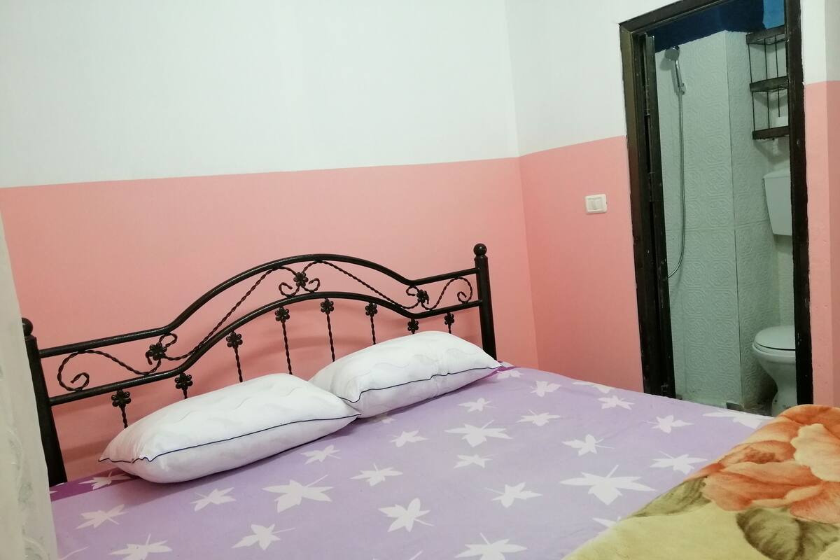 A bed with a floral-patterned bedspread and two pillows, a black metal headboard, and a pink and white wall.