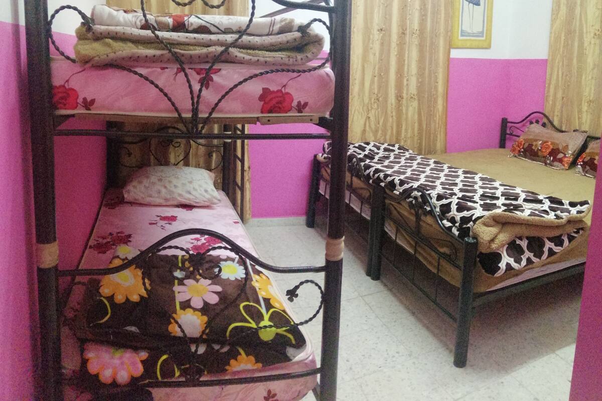 A bunk bed with a pink and floral bedspread, a lower bunk with a floral-patterned blanket, and a single bed with a patterned bedspread.