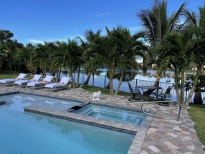 Uma piscina com espreguiçadeiras, um pequeno ofurô e palmeiras.