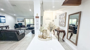 A spacious living area with a white central table, a kitchen sign, and a large mirror.