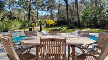 Een houten terras met een pooltafel en stoelen, omgeven door bomen en begroeiing.