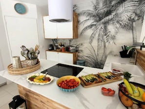 A kitchen with a central island, a clock on the wall, and a tropical mural.