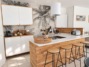 A modern kitchen with a central island, bar stools, and a wall-mounted light fixture.