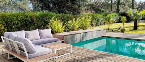 A wooden deck with a pool, surrounded by greenery and trees.