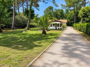 A pathway leading to a house with a pool, surrounded by greenery and trees. - Villa Le Bordelou, Heated Pool, Lacanau Ocean (Lacanau Océan)