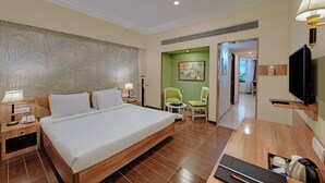 A hotel room with a large bed, bedside tables with lamps, a desk with a chair, a television, and a green accent wall.
