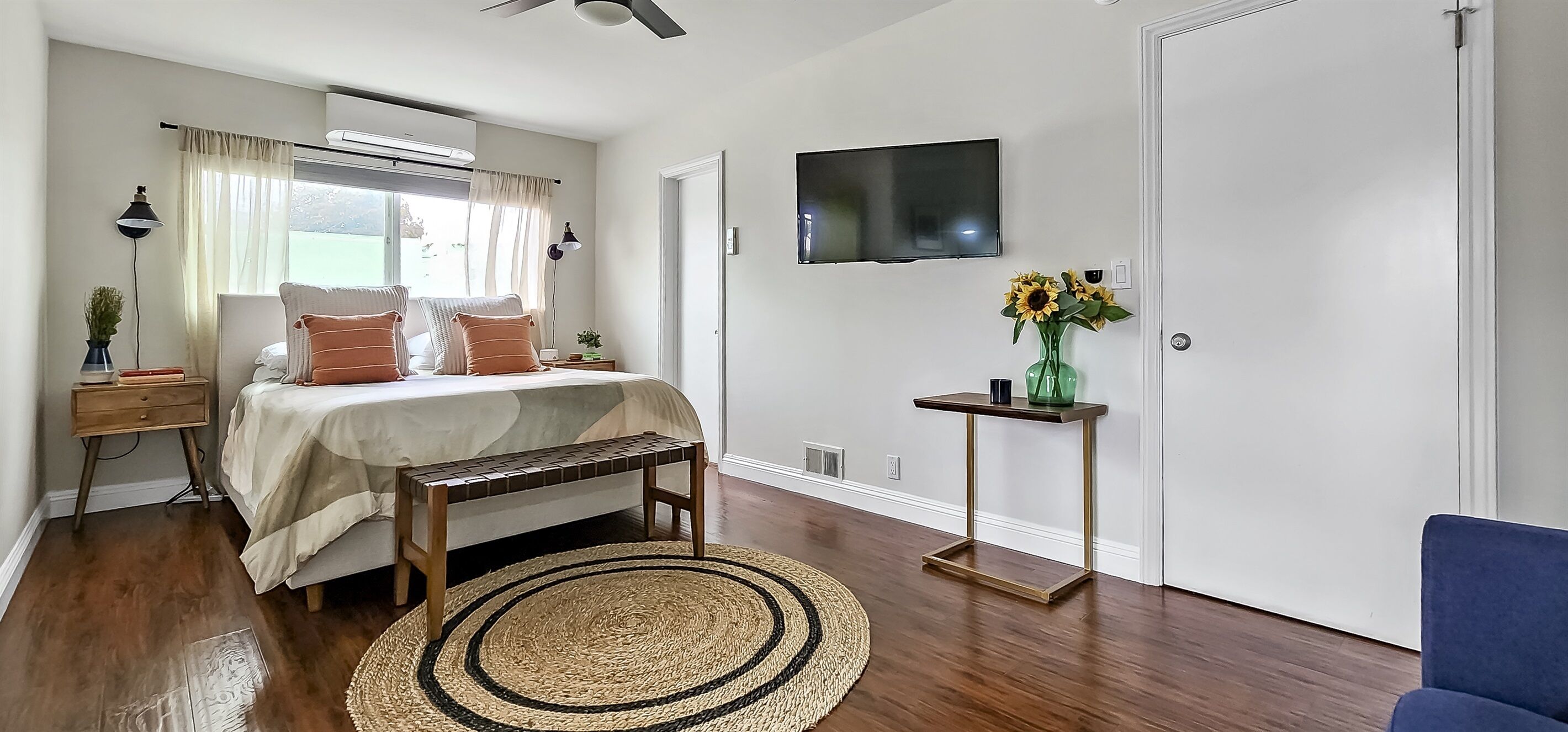 Een slaapkamer met een bed, nachtkastjes, een televisie, een raam en een deur.