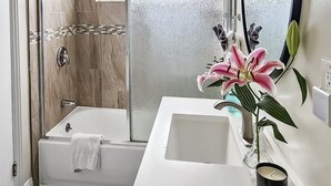 Une salle de bain moderne équipée d’une douche, d’une baignoire et d’un meuble-lavabo avec un miroir et un vase de fleurs.