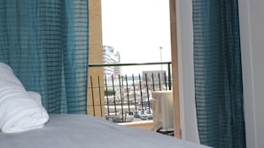 A hotel room with a bed, a window with blue curtains, and a view of the cityscape. - La finestra sul porto (Palermo)