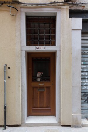 Ein Gebäudeeingang mit einer Holztür, einem Fenster mit Metallgitter und einem Schild mit der Aufschrift "5091A".