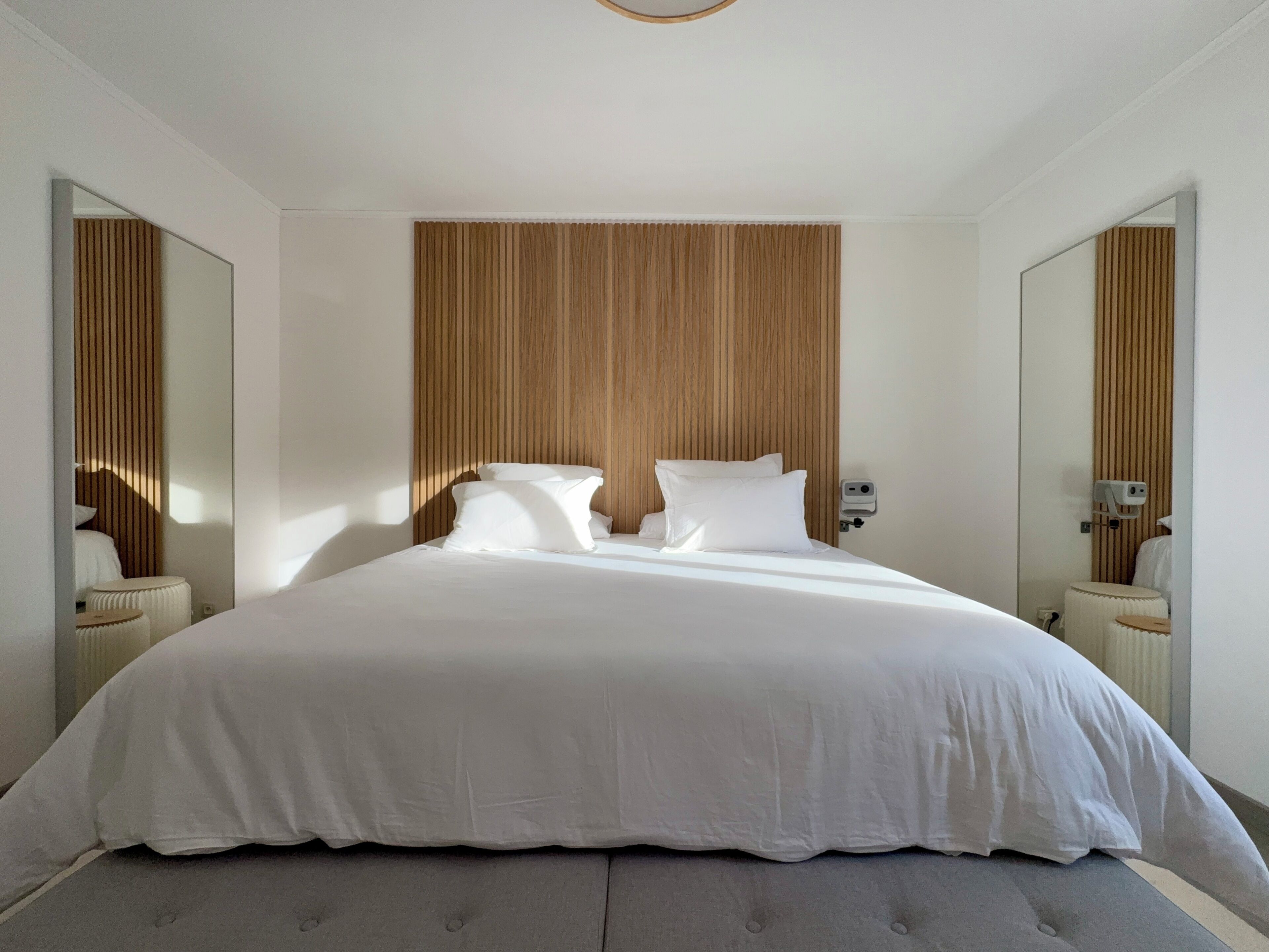 Una cama grande con cabecera de madera, dos mesitas de noche y un espejo a cada lado.