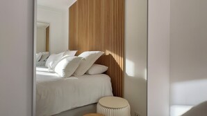 Een slaapkamer met een bed, kussens, een wand van houten latten en een ronde stoel.