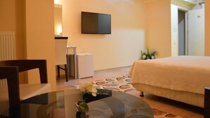 Habitación de hotel con cama, televisor montado en la pared, una mesita con un florero y una silla.