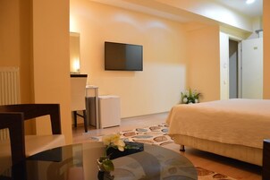 Habitación de hotel con cama, televisor montado en la pared, una mesita con un florero y una silla.