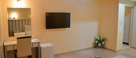 Una habitación con escritorio, silla, radiador, televisor y una planta pequeña.