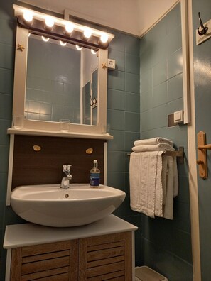A bathroom with a white sink, a mirror with lights, a bottle of hand soap, and a towel rack. - Hotel Saint-Quay (Saint-Quay-Portrieux)