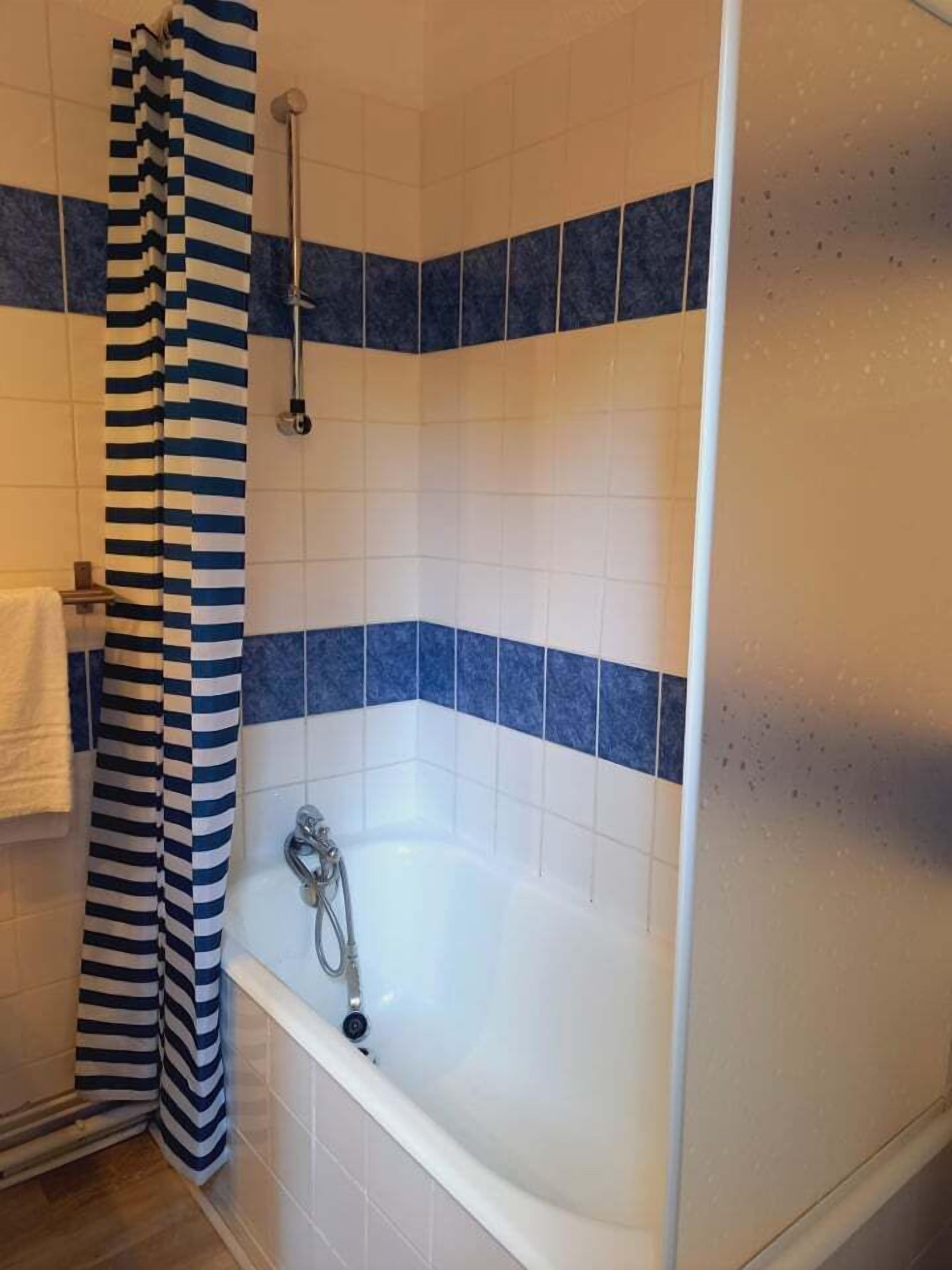 A bathroom with a bathtub, blue and white tiles, and a striped shower curtain.