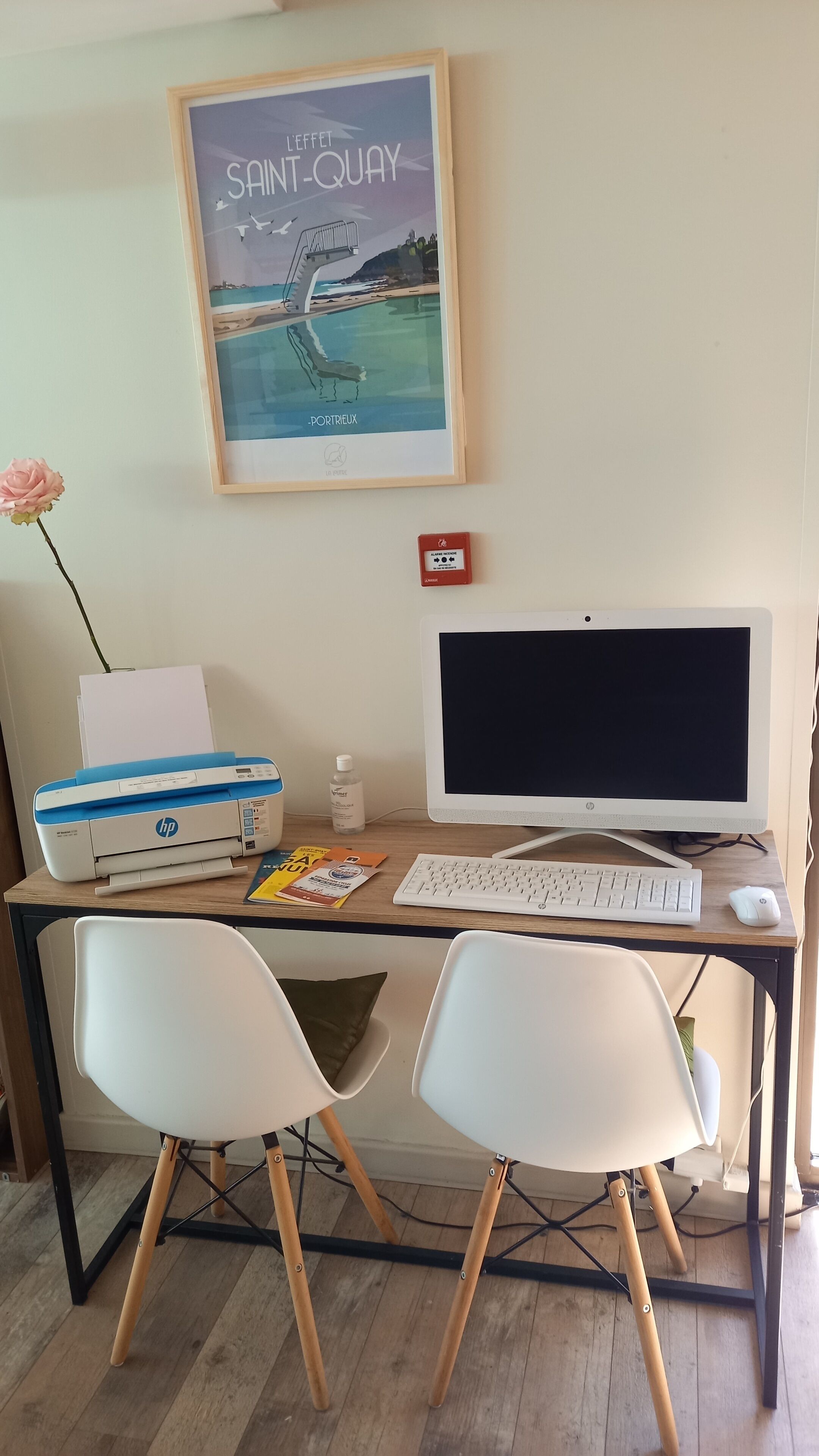 A home office setup with a desktop computer, two white chairs, a printer, and a framed picture on the wall.