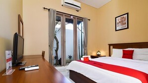 Ein Hotelzimmer mit Bett, Fernseher, Schreibtisch und einem fensterbepflanzten Fenster.