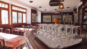 A bar area with multiple tables and chairs, a large display of empty glasses, and a sign indicating a toilet nearby. - Hotel du Doron (Beaufort)