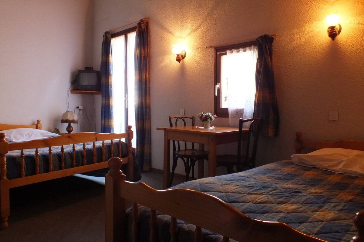 A room with two wooden beds, a small table with chairs, and a television on a shelf.