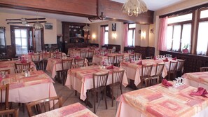 Un restaurante con varias mesas dispuestas para comer, sillas de madera y una araña.