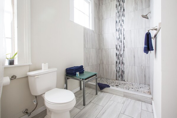 A bathroom with a toilet, a shower with a tiled wall, and a small table with towels.