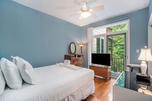 Un dormitorio con cama, televisión, cómoda, lámpara y ventana con vista a follaje.