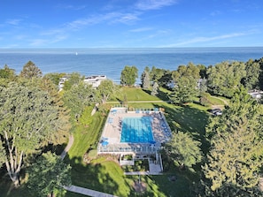 Vista aérea de una propiedad con piscina rodeada de árboles, vistas despejadas al mar y un césped bien cuidado.