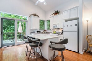 Cocina moderna con armarios blancos, una isla central con taburetes de bar, un refrigerador y vistas a un balcón con mobiliario exterior.