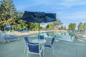Zona de piscina con sillas de descanso, una mesa y sombrillas.