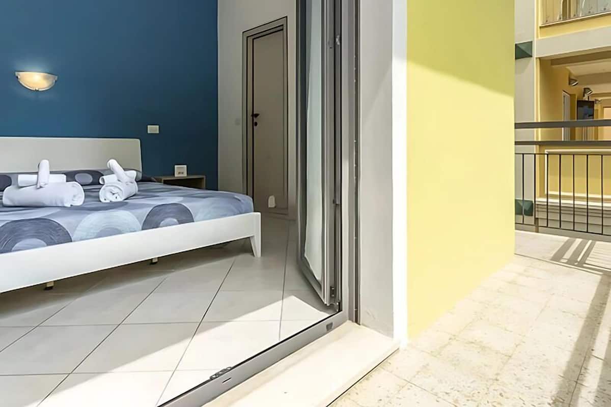 A modern bedroom with a bed, a nightstand, and a wall-mounted light fixture.