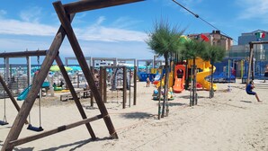 A beach playground with swings and slides, surrounded by sand and a few people. - Hotel Italy (Misano Adriatico)