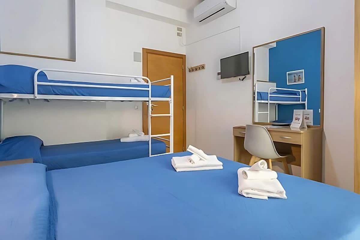 A hotel room with bunk beds, a desk with a chair, a TV, and a mirror.