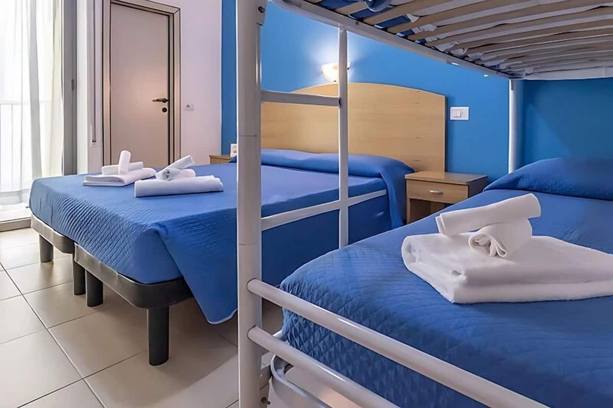 A hotel room with bunk beds, a wooden headboard, a bedside table, and a window with curtains.