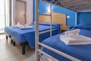 A hotel room with bunk beds, a wooden headboard, a bedside table, and a window with curtains. - Hotel Italy (Misano Adriatico)
