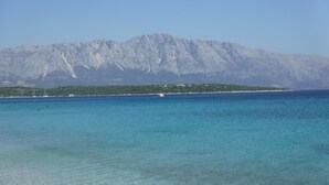 Une vue sur la côte, avec une eau turquoise et limpide, une chaîne de montagnes lointaine et une petite île à la végétation clairsemée.