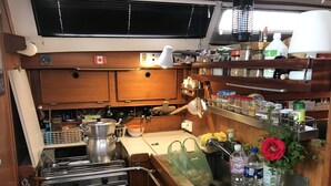 Une cuisine compacte équipée d’une cuisinière, d’un four et de divers ustensiles de cuisine. On y trouve un évier avec un robinet, un plan de travail orné d’un vase de fleurs et une étagère avec des bocaux et des bouteilles.