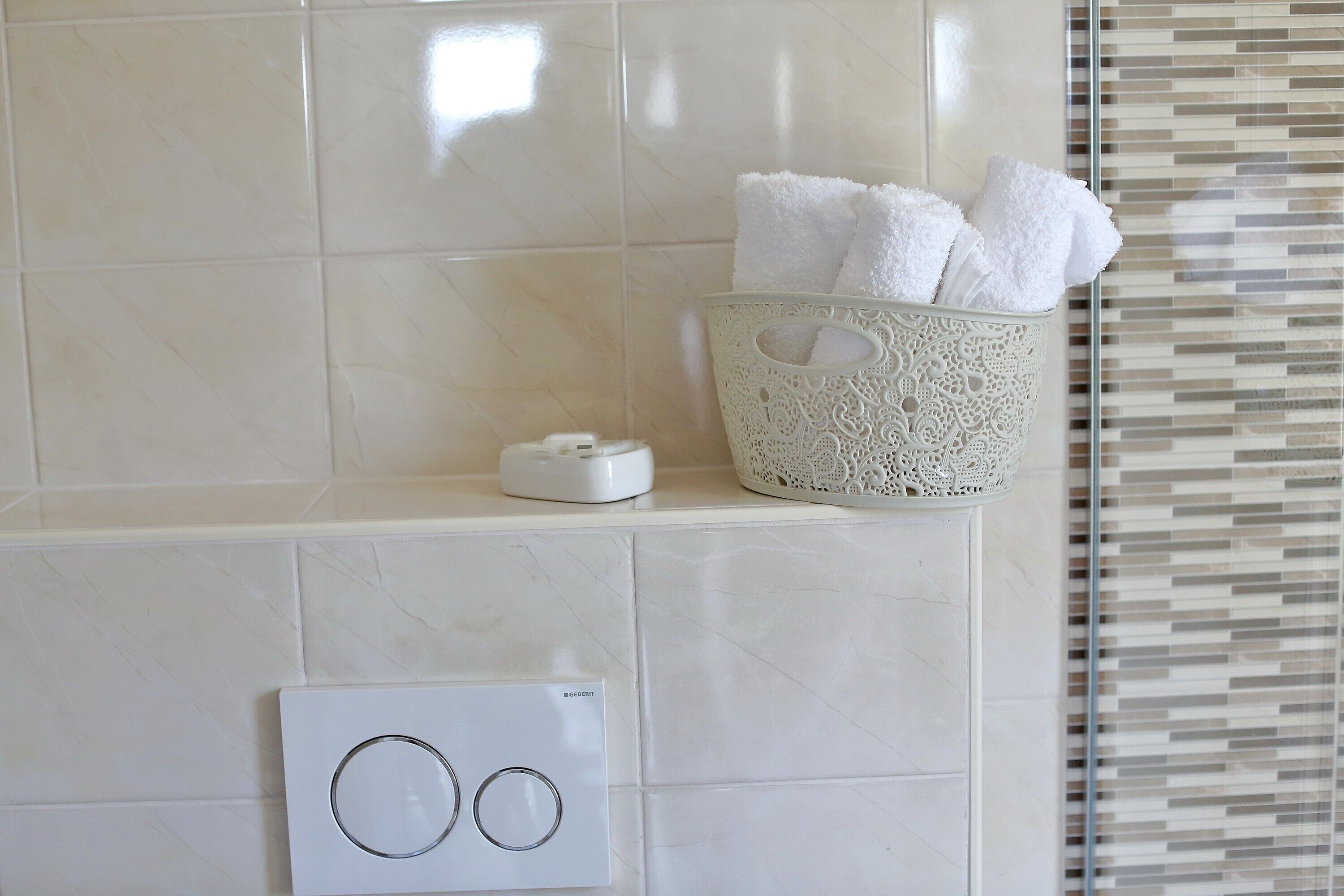 A bathroom with a white tiled wall, a thermostat, and a decorative basket with towels.