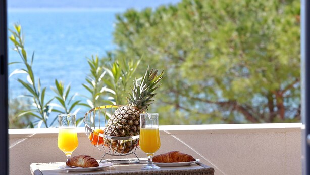 En morgenmadsopstilling med ananas, croissanter og appelsinjuice på en balkon med udsigt over havet.