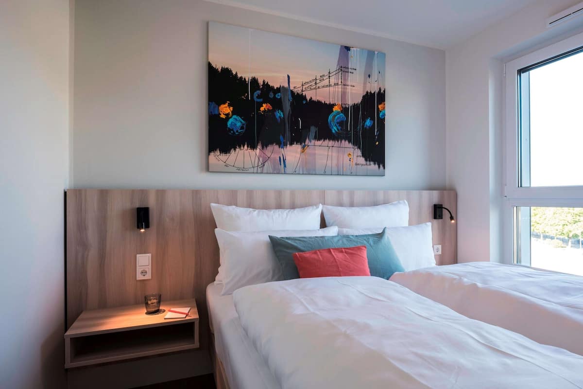 Quarto de hotel com uma cama, mesa de cabeceira e um quadro na parede.