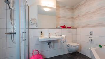 Ein modernes Badezimmer mit Duschkabine aus Glas, einem weißen Waschbecken mit Spiegel darüber, einer Toilette und einer Badewanne.