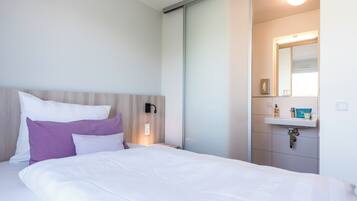 A hotel room with a bed, a nightstand, a wall-mounted lamp, a bathroom with a sink and mirror.