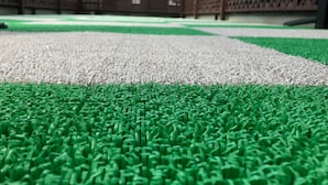 Primer plano de césped artificial con una sección blanca y verde, rodeada por una valla marrón.