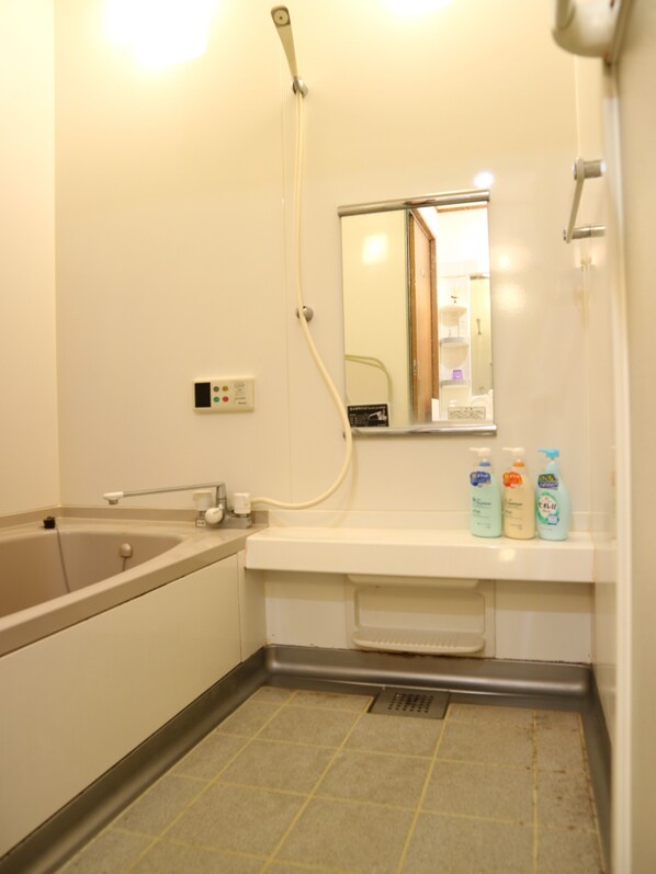 Une salle de bain avec une baignoire, un lavabo, un miroir et trois bouteilles de savon posées sur le comptoir.