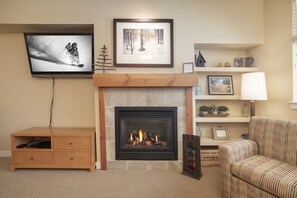 A living room with a fireplace, a television mounted on the wall, a wooden cabinet, and a striped armchair.