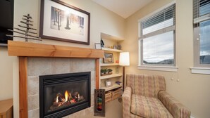 A living room with a fireplace, a striped armchair, a bookshelf, and a window with blinds. - Top Floor Mountain Retreat, Prime Location to WP Base Village, Trestle Bike Park (Winter Park)